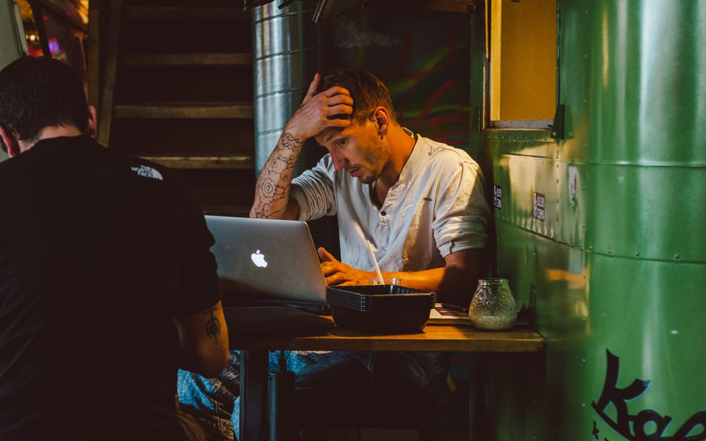 Tattoo guy sitting in a bar with Mac laptop scratching head