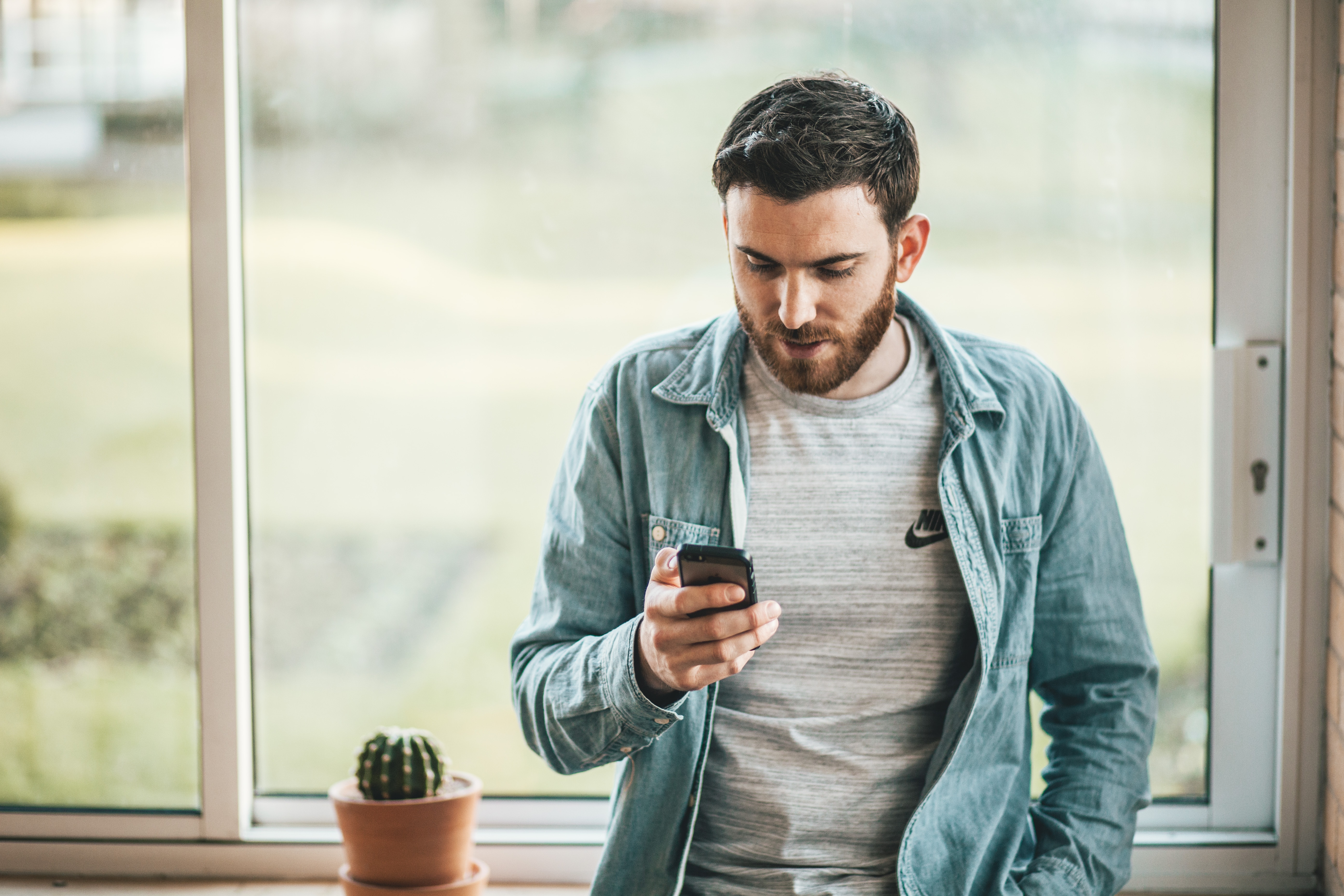 Man holding phone standing by a window